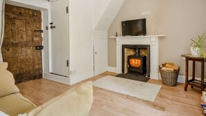 A living room with a fireplace, a television above it, a wooden door, and a white wall. - 1 Bed in Brecon (oc-88748) (Trallong)