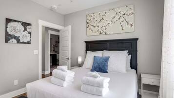 Una cama bien tendida con sábanas y toallas blancas, un cabecero de madera oscura y una obra de arte floral colgada en la pared.