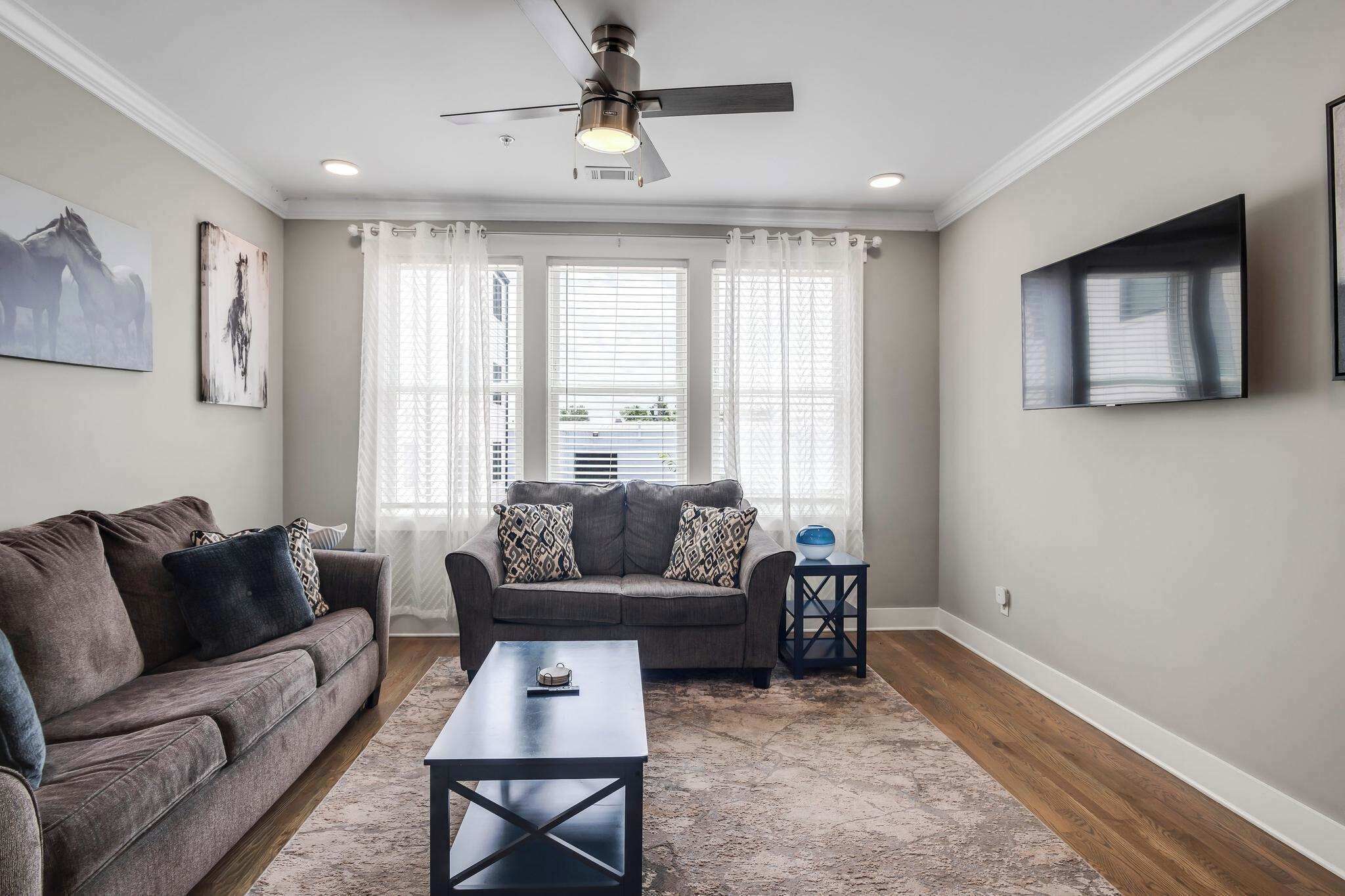 A living room with a sofa, a coffee table, a ceiling fan, and a TV mounted on the wall.