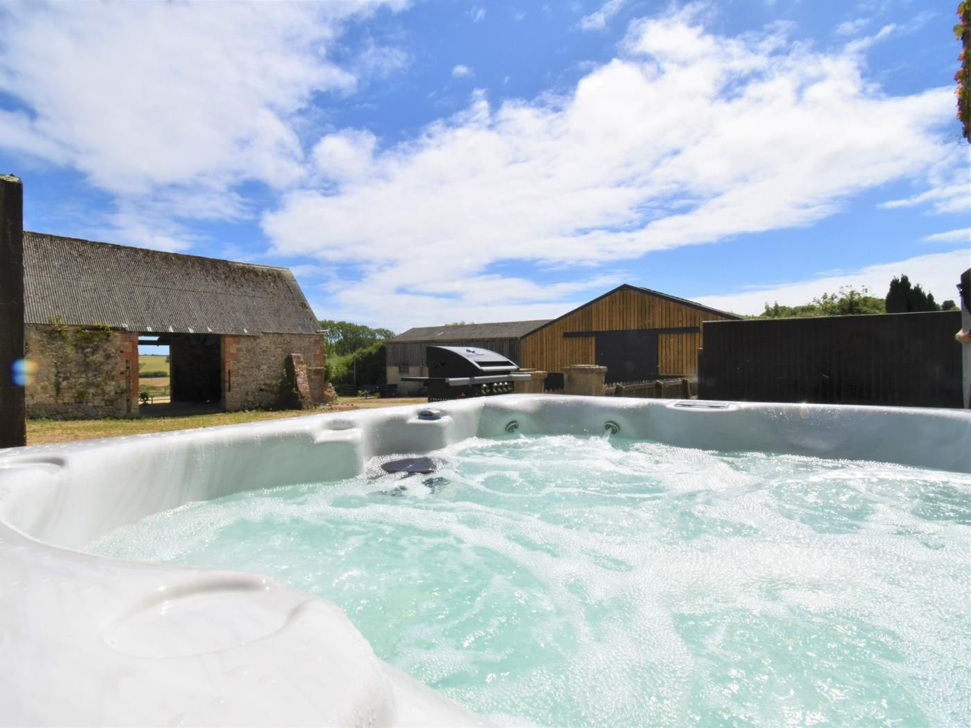 A hot tub in a rustic outdoor setting with wooden buildings and a clear sky.