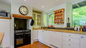 A kitchen with a built-in oven, a microwave, wooden cabinets, and a window with a view of greenery. - 3 Bed in Ambleside (oc-88769) (Claife)