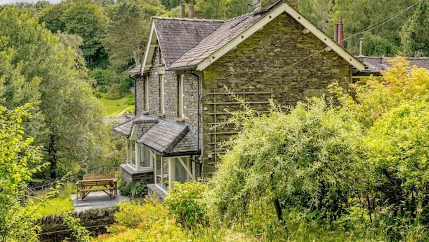 A stone building with a gabled roof, surrounded by lush greenery. - 3 Bed in Ambleside (oc-88769) (Claife)