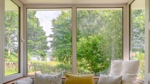 A room with a large window, a built-in bench with cushions, and a view of a green landscape. - 3 Bed in Ambleside (oc-88769) (Claife)