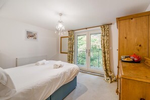 A bedroom with a bed, a radiator, a chandelier, a wardrobe, and a view of greenery through a door. - 3 Bed in Ambleside (oc-88769) (Claife)