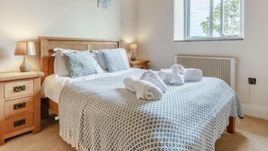 A bedroom with a wooden bed, two bedside tables with lamps, a radiator, and a window with a view. - 2 Bed in Launceston (oc-88859) (Saint Giles on the Heath)