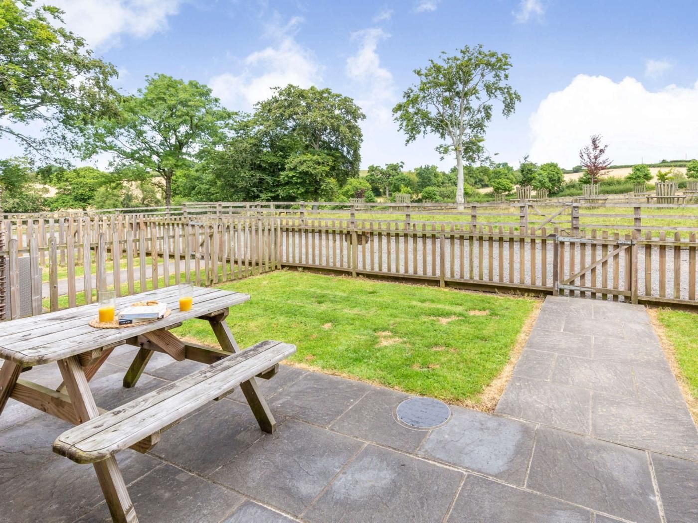 A picnic table with a glass of orange juice and a box of snacks, set on a stone patio with a wooden fence in the background.