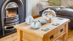 A cozy living room with a fireplace, a wooden coffee table with tea sets, and a leather sofa. - 2 Bed in Launceston (oc-88859) (Saint Giles on the Heath)