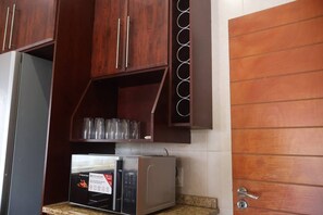 A kitchen with wooden cabinets, a microwave, and a shelf with glasses. - Room-luxurious Room - D (Johannesburg)