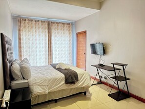 A hotel room with a bed, a TV, a desk, and a door. - Room-luxurious Room - D (Johannesburg)