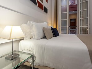 Ein Hotelzimmer mit Bett, Nachttisch mit Lampe und Blick durch ein Fenster nach draußen.