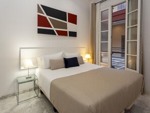 Une chambre d’hôtel avec un lit, des lampes de chevet, une table d’appoint en verre, un grand tableau abstrait et une vue par la fenêtre.