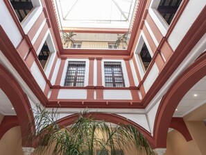 Ein mehrgeschossiges Atrium mit einem offenen zentralen Bereich, großen Fenstern mit Metallstreben und einem Blumentopf im Vordergrund.