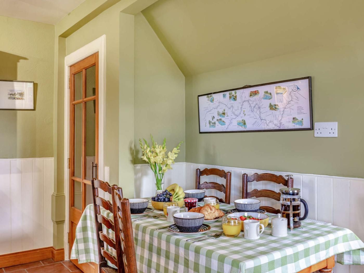 A dining area with a table set for breakfast, chairs, a wall-mounted map, and a door.