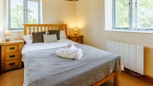A bedroom with a wooden ceiling, a bed with a white headboard, two bedside tables with lamps, and a window with a view of trees. - 3 Bed in Launceston (oc-88858) (Saint Giles on the Heath)