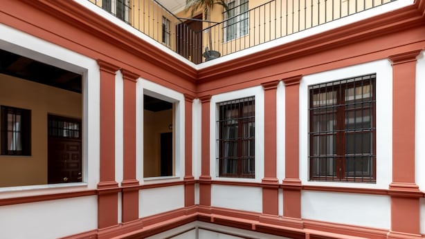 Un edificio con fachada roja y blanca, varias ventanas con rejas y un balcón con barandilla.