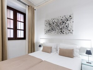 Ein Hotelzimmer mit einem Bett, einem Vorhangfenster, einem Wandbild und einem Nachttisch mit Lampe.