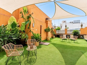 Eine Dachterrasse mit Kunstgrashalm, Korbmöbeln, Topfpflanzen und einem großen Sonnenschirm.