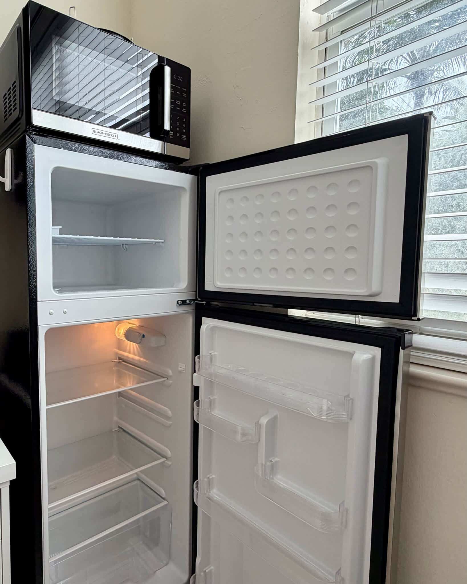 An open refrigerator with a microwave on top, a freezer compartment, and a door with a handle.