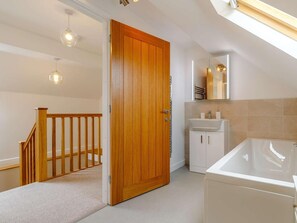 Ein modernes Badezimmer mit Holztür, Waschbecken in Weiß, Spiegel und Badewanne.