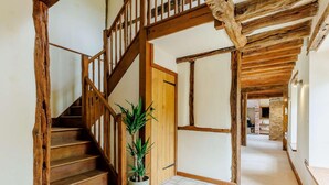 Un escalier en bois orné d’un pot de fleurs, une porte et un couloir aux poutres apparentes.