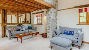 Un salon chaleureux avec un mur en pierre, des poutres apparentes, un canapé gris et une table basse.