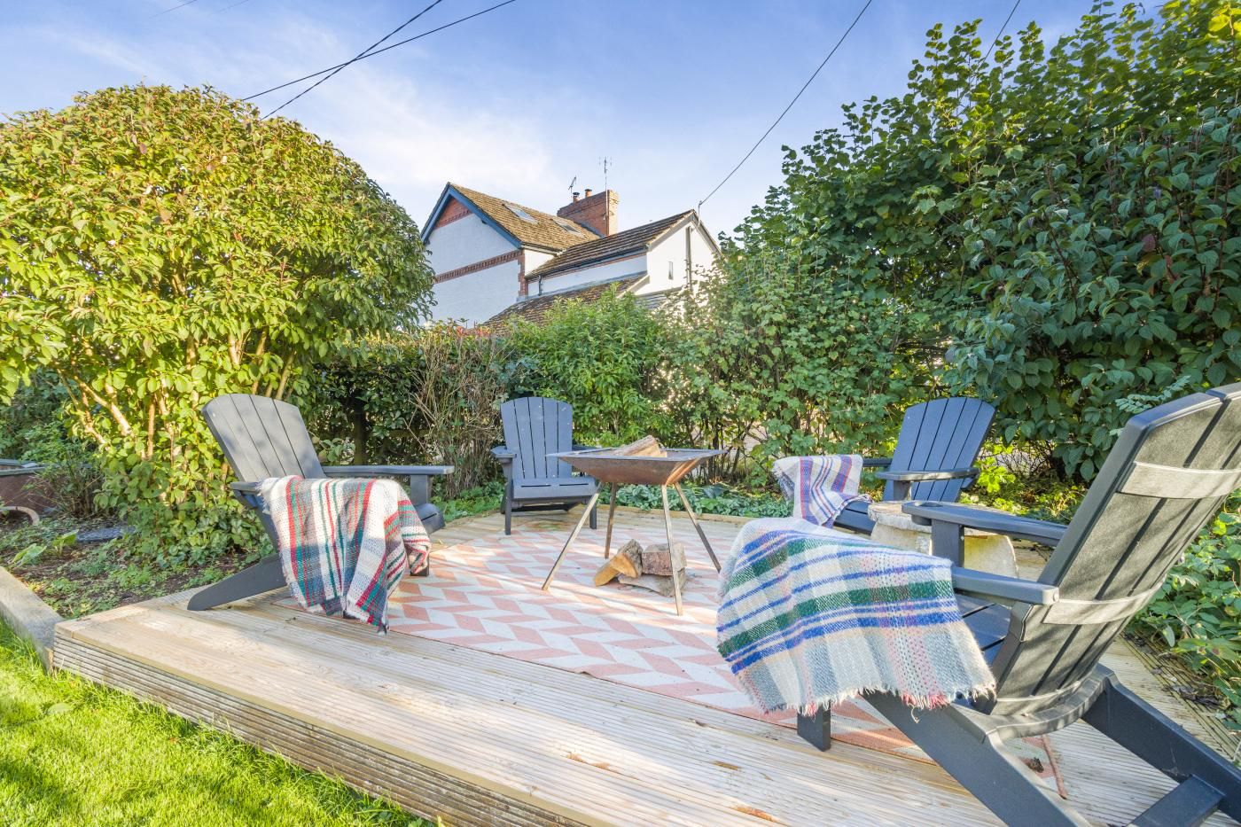 Un patio con mobiliario exterior, una terraza de madera y una casa al fondo.