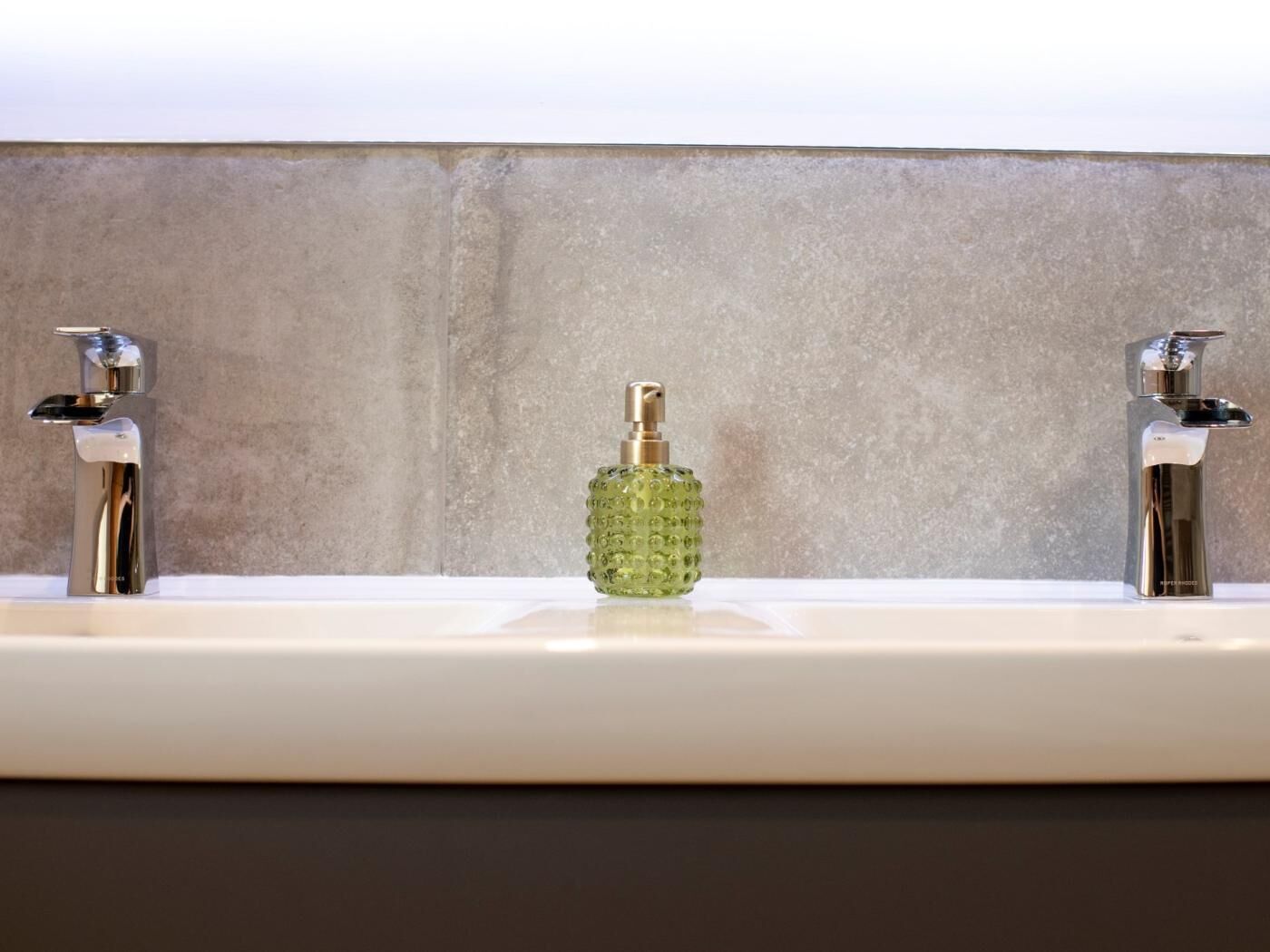 A bathroom with two chrome faucets and a central soap dispenser.