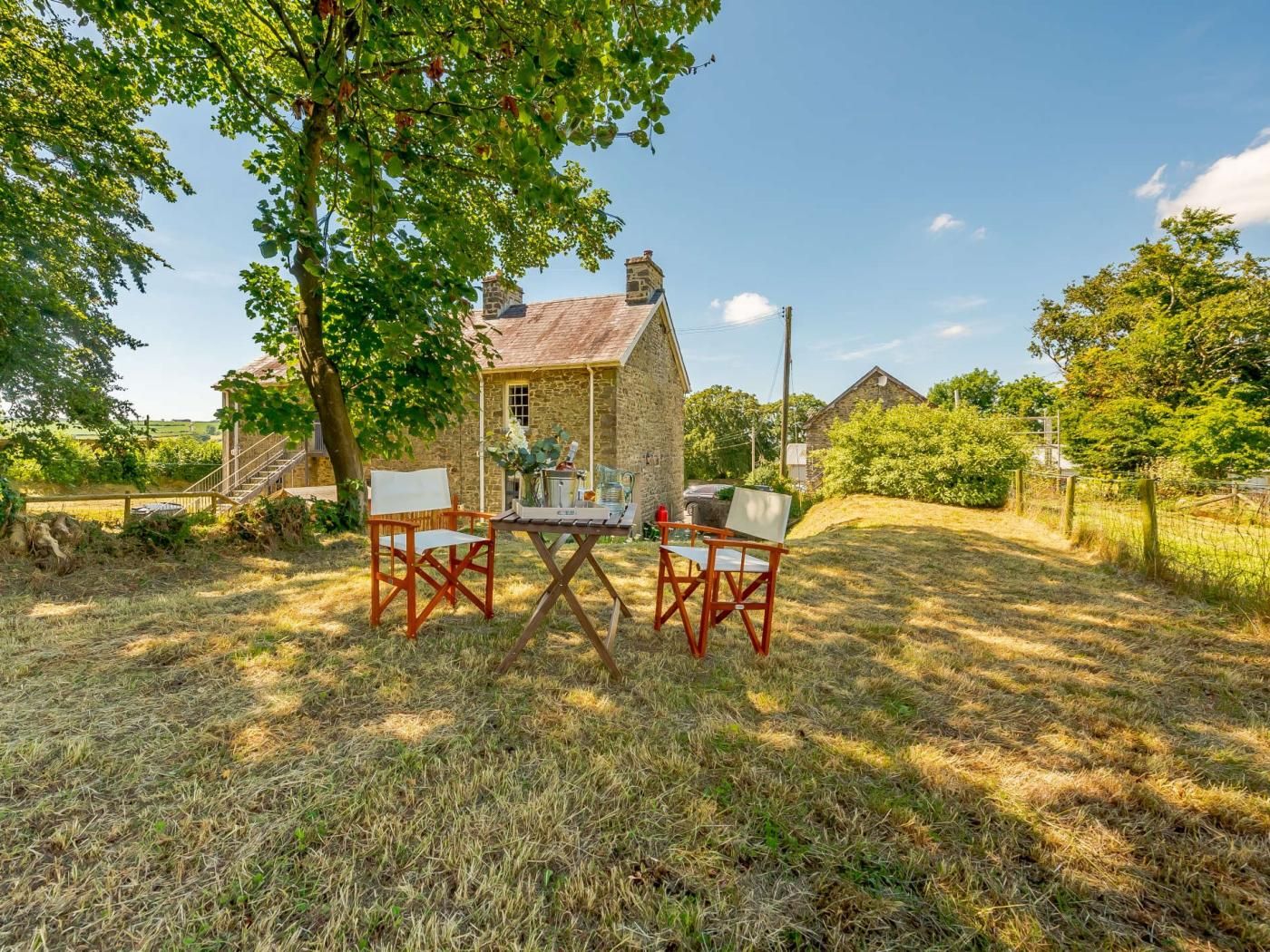 A stone cottage with a small table and two chairs in a grassy area.