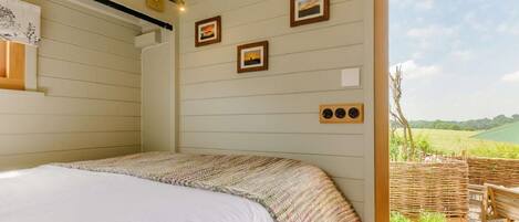 A bedroom with a bed, a wooden ceiling, and a view of a garden.