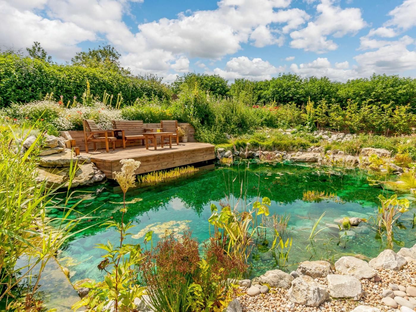 A clear pool with a wooden deck and seating area surrounded by lush greenery.