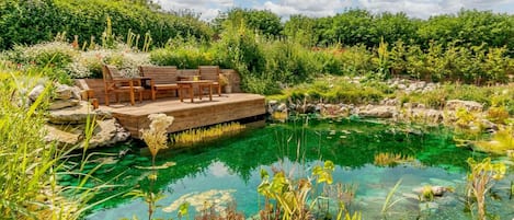 A clear pool with a wooden deck and seating area surrounded by lush greenery.