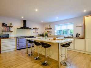 A modern kitchen with a central island, bar stools, a stove, and a window with a view. - 4 Bed in Melton Constable (oc-88678) (Briningham)