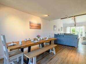 A modern living room with a wooden dining table, benches, a blue sofa, and a cityscape painting on the wall. - 4 Bed in Melton Constable (oc-88678) (Briningham)