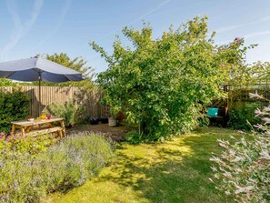A backyard with a wooden fence, a table with drinks, and a variety of plants. - 4 Bed in Melton Constable (oc-88678) (Briningham)