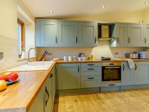 A kitchen with light blue cabinets, a wooden countertop, a sink, a stove, and a window with blinds. - 3 Bed in Usk- (oc-87286) (Llandenny)