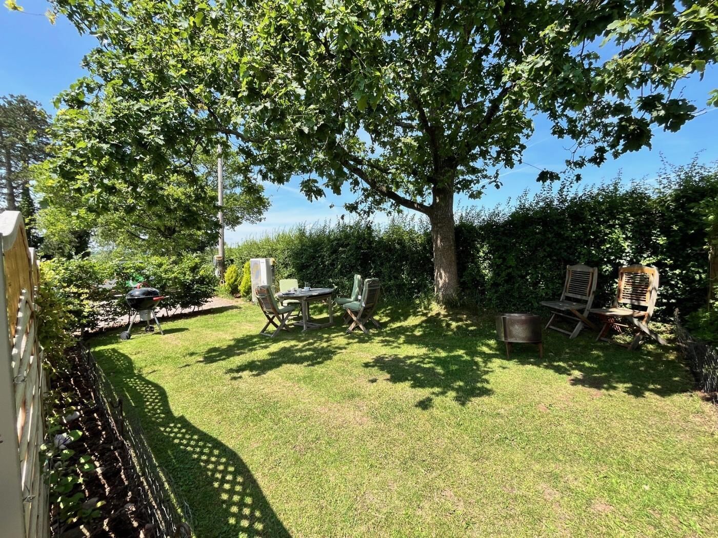 Un jardin avec une pelouse, une table, des chaises et un barbecue.