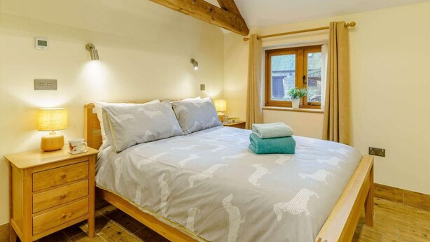 Een slaapkamer met een houten bed, een nachtkastje met een lamp, een raam met gordijnen, en een kleine bloempot op de vensterbank.
