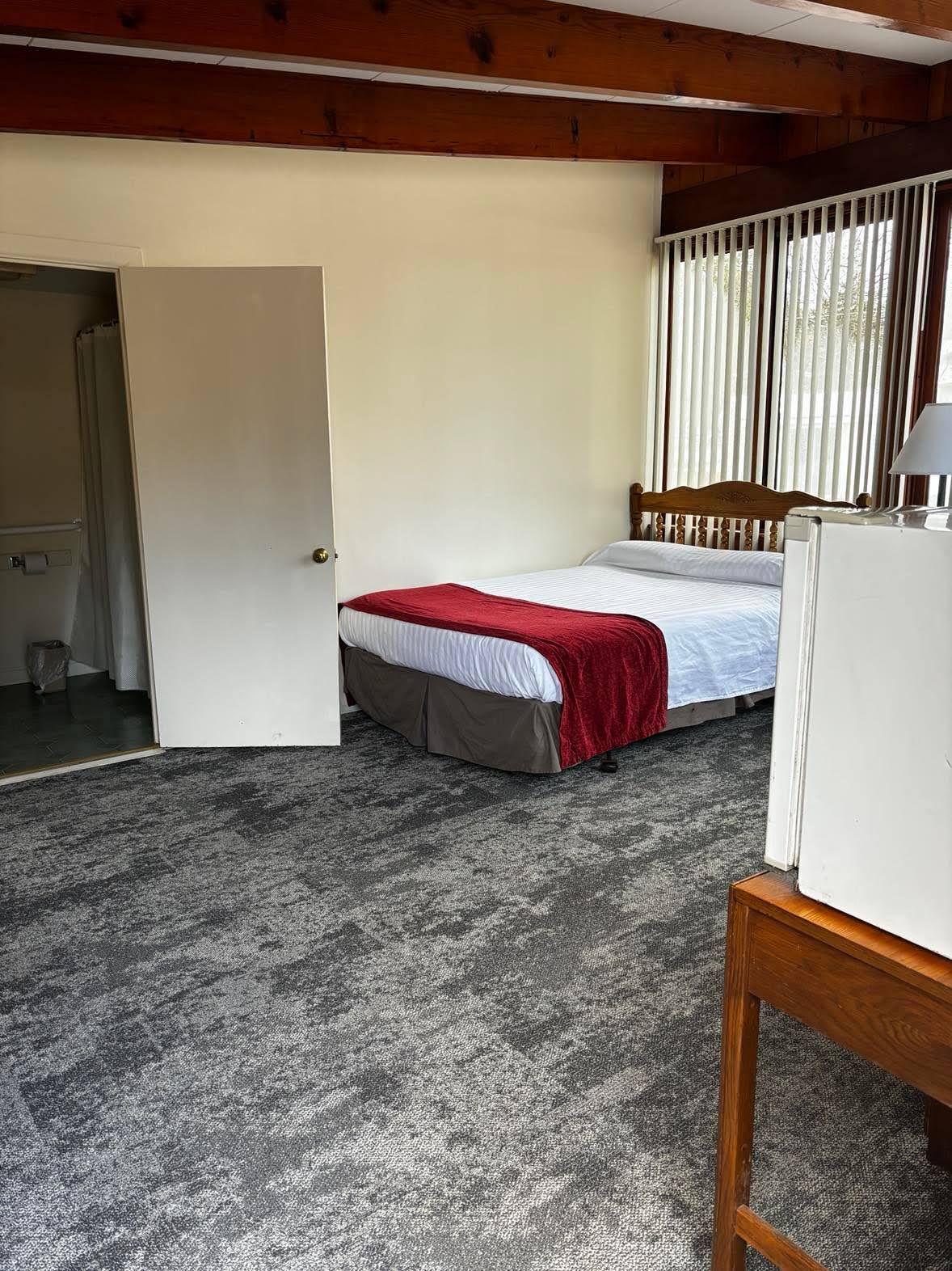 Un dormitorio con cama, una puerta que da a otra habitación y una ventana con persianas.