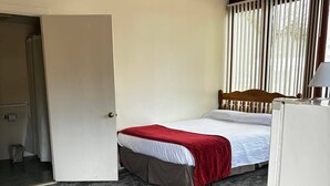 A bedroom with a bed, a door leading to another room, and a window with blinds. - Cozy 1-bedroom hotel room, Hamilton - #306 Mohawk (Hamilton)