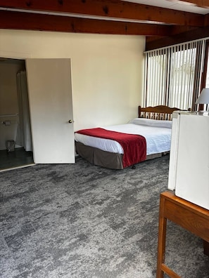 Un dormitorio con cama, una puerta que da a otra habitación y una ventana con persianas.