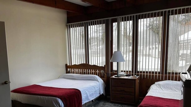 A room with two beds, a nightstand, a lamp, and a window with blinds. - Cozy 1-bedroom hotel room, Hamilton - #306 Mohawk (Hamilton)