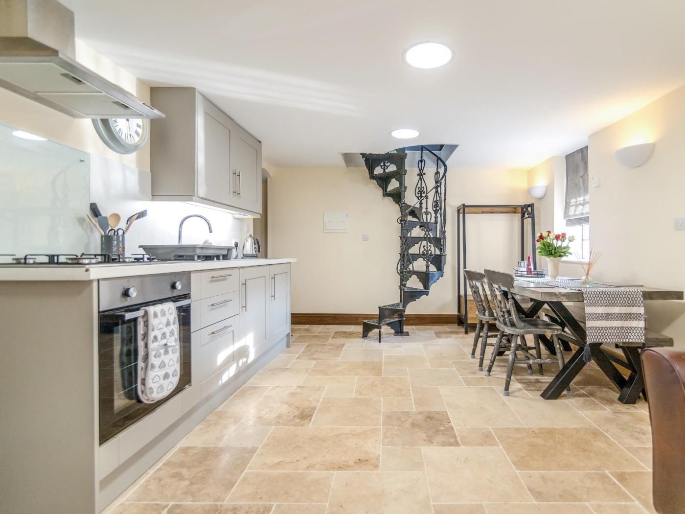 A modern kitchen with a central island, a dining area with a table and chairs, and a spiral staircase.