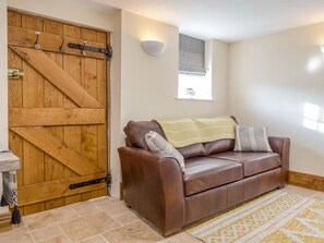 A room with a brown leather sofa, a wooden door with metal hinges, a small window with a blind, and a wall-mounted light fixture. - 1 Bed in Hereford (oc-87736) (Monnington on Wye)
