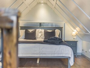 Une chambre avec un plafond en pente, un lit avec des oreillers, une table de chevet avec une lampe et un plancher en bois.