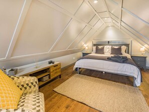 Ein Schlafzimmer mit schräg stehender Decke, einem Bett mit vielen Kissen, einem Nachttisch und einem kleinen Holzschrank.