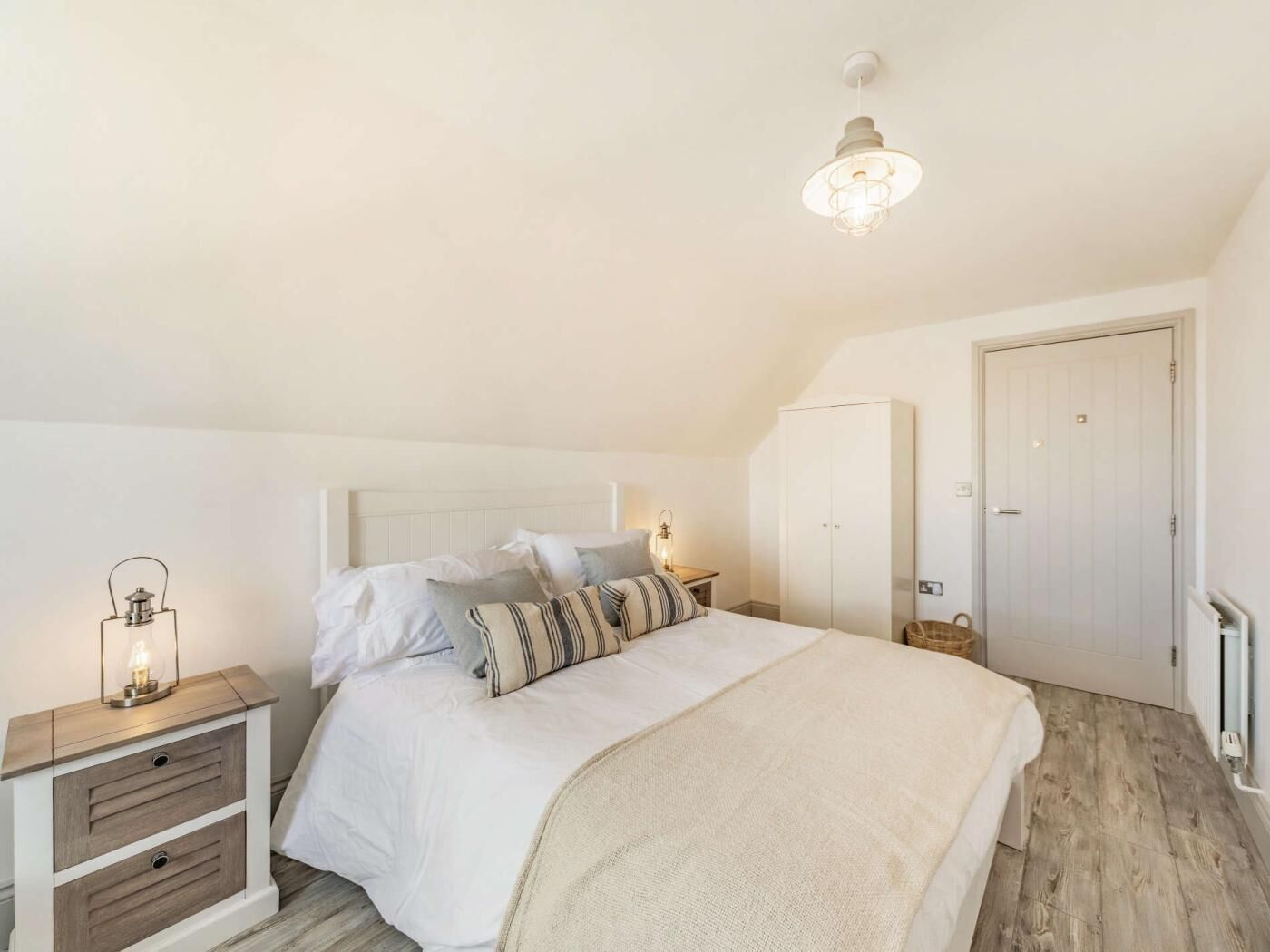 Een slaapkamer met een bed, nachtkastje, lamp, kledingkast en een plafondlamp.
