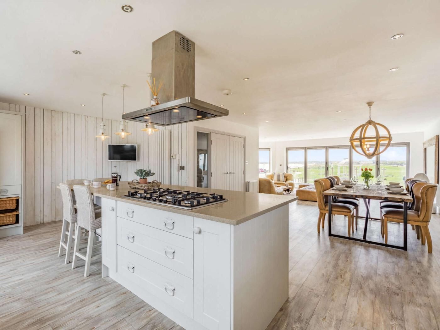 A modern kitchen with a central island, white cabinetry, and a dining area with a large table and chairs.