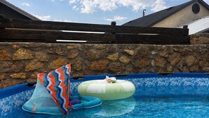 Una piscina con due cerchi gonfiabili, un muro in pietra e un edificio con tetto spiovente sullo sfondo.