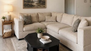 Un soggiorno con un divano angolare beige, un tavolino da caffè nero, una lampada e una ventola a soffitto.