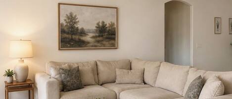 A living room with a beige sectional sofa, a black coffee table, a lamp, and a ceiling fan.